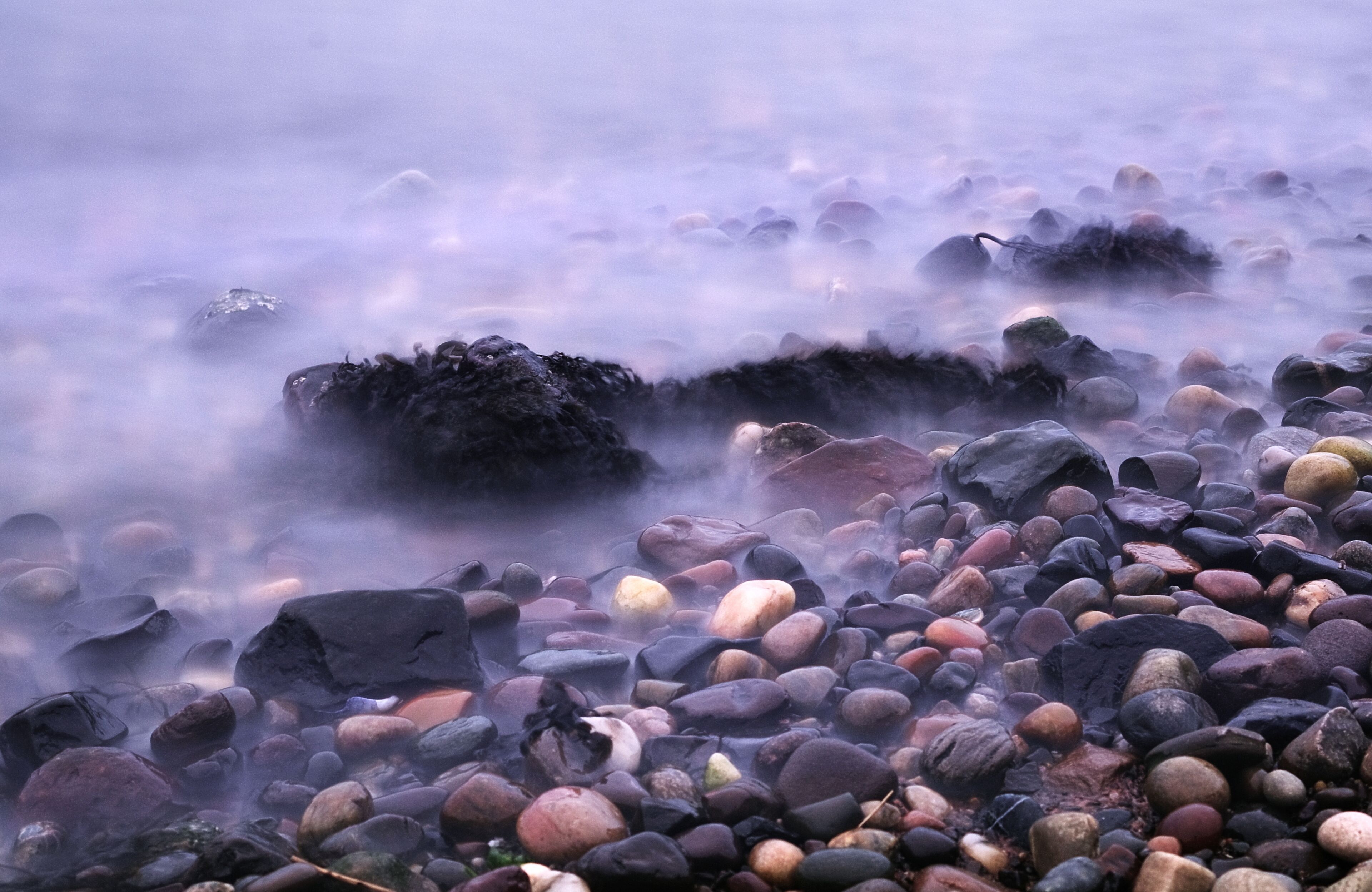 Una costa rocosa con piedras de diferentes tamaños y un ambiente brumoso.