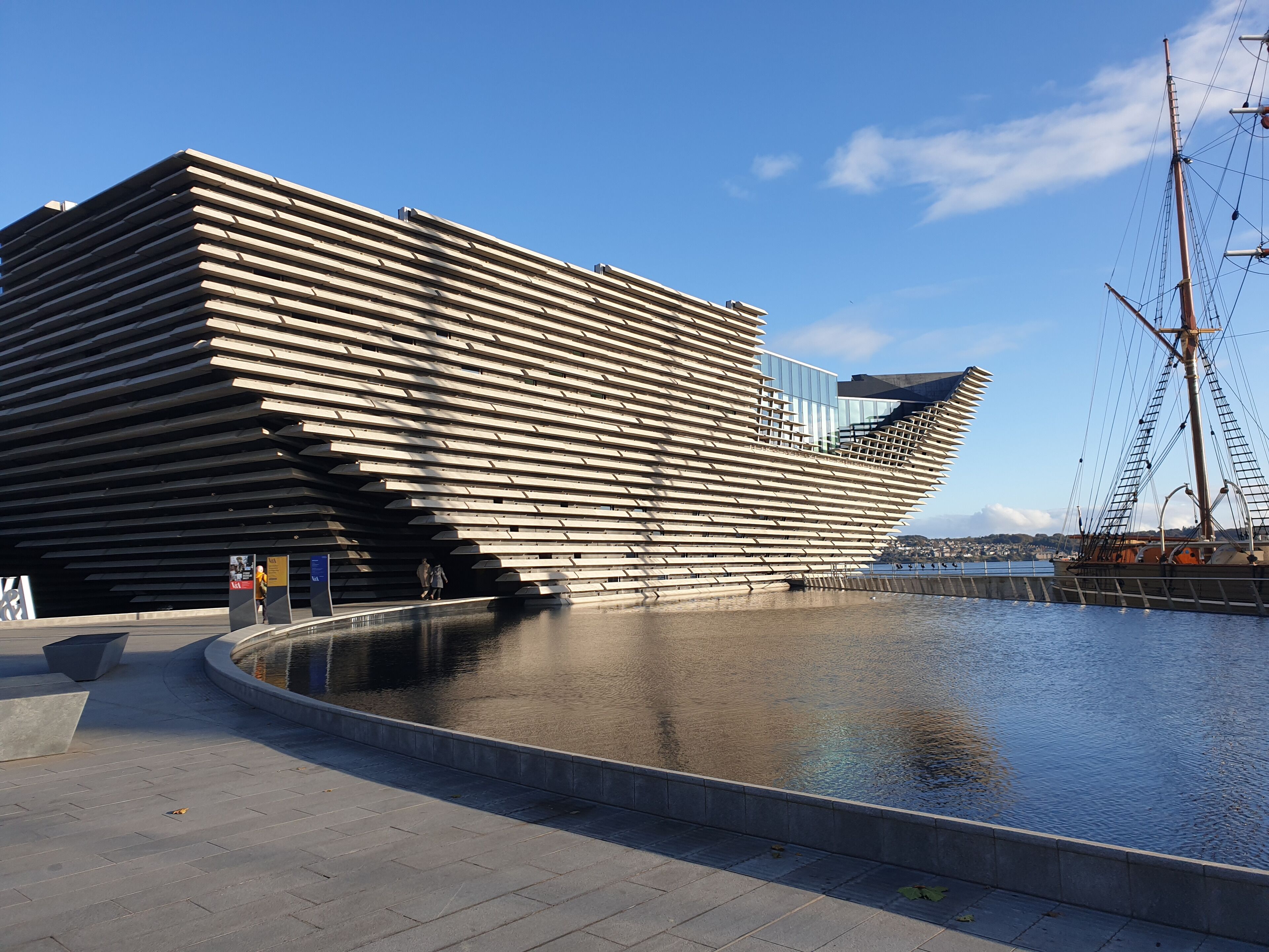 A modern architectural building with a unique slatted design, situated beside a waterfront.
