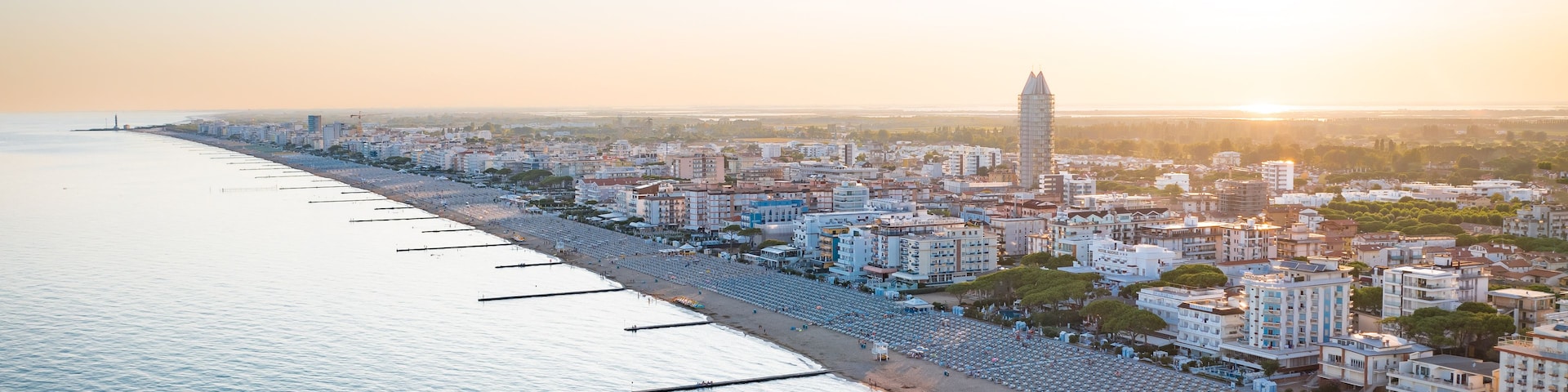 Un paysage urbain côtier avec une tour imposante, une longue plage bordée de parasols et une mer calme.