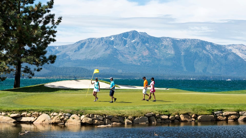 A golf course with a lake and mountains in the background.