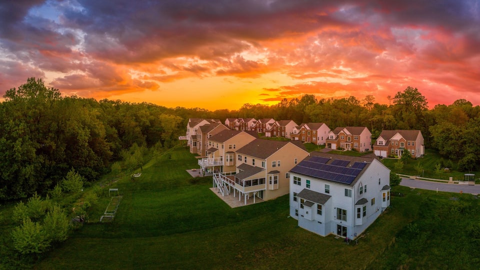 A residential area with houses and a road, surrounded by trees, during sunset.