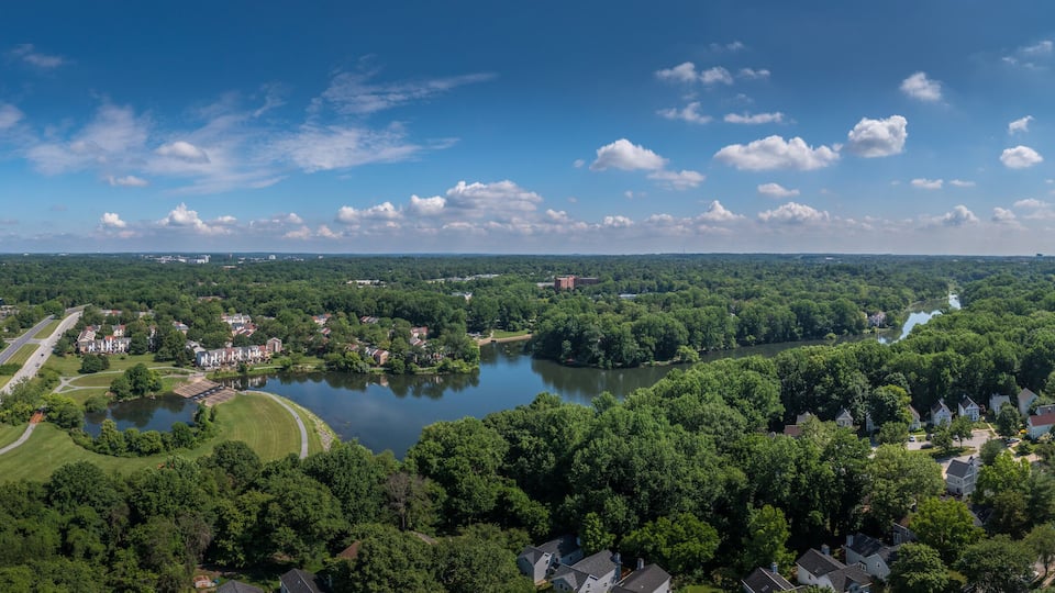 A river winding through a densely wooded area with residential houses and a highway.