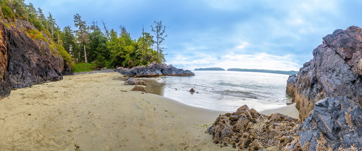 A rocky coastline with a sandy beach, dense forest, and calm sea.