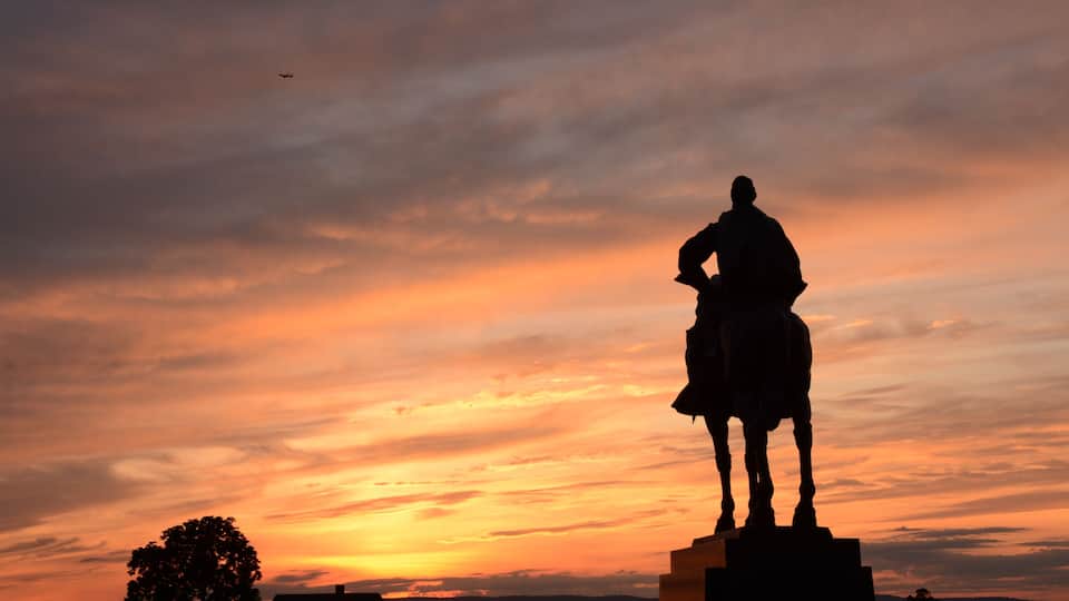 A statue of a man on horseback against a sunset sky.