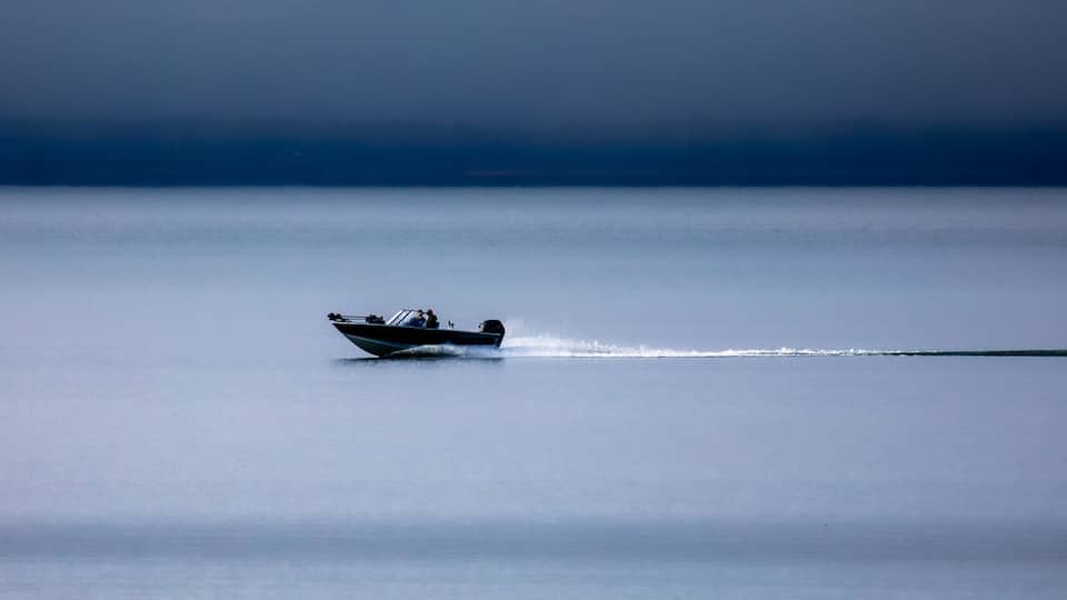 A single motorboat on a calm body of water with a uniform horizon.
