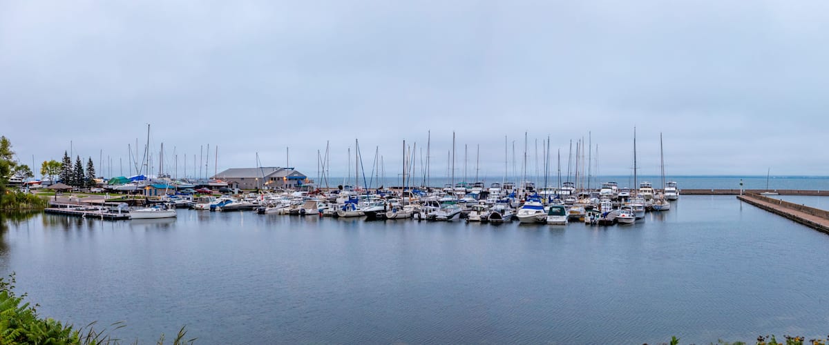 A marina with numerous sailboats docked, a pier, and a building with a blue roof.