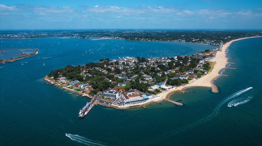 Vue aérienne d’une ville côtière avec une plage, une jetée et un navire de croisière amarré dans le port.