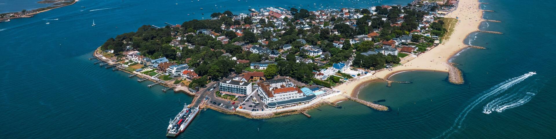 An aerial view of a coastal town with a beach, a pier, and a cruise ship docked at the harbor.
