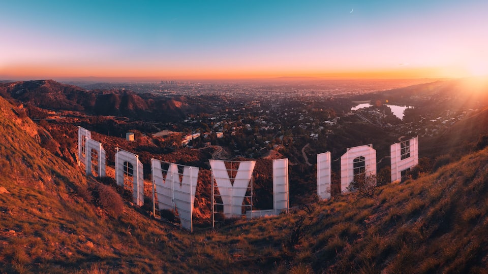 A mountainous landscape with a city in the valley below, featuring prominent white structures with the letters 'HOWY IN'.