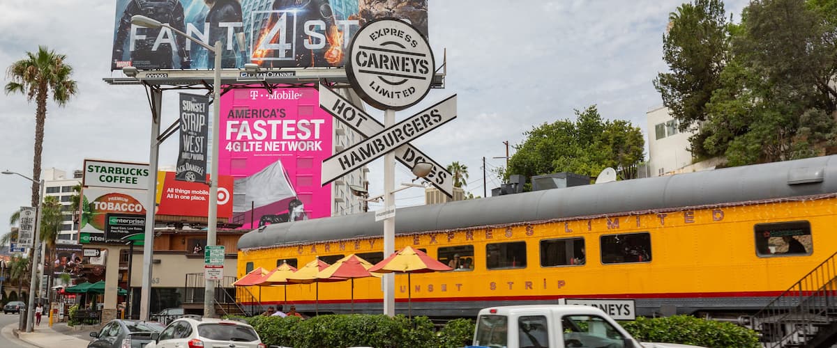 A busy street with a yellow train, a billboard for Marvel's FANT4ST, and a sign for Carneys.