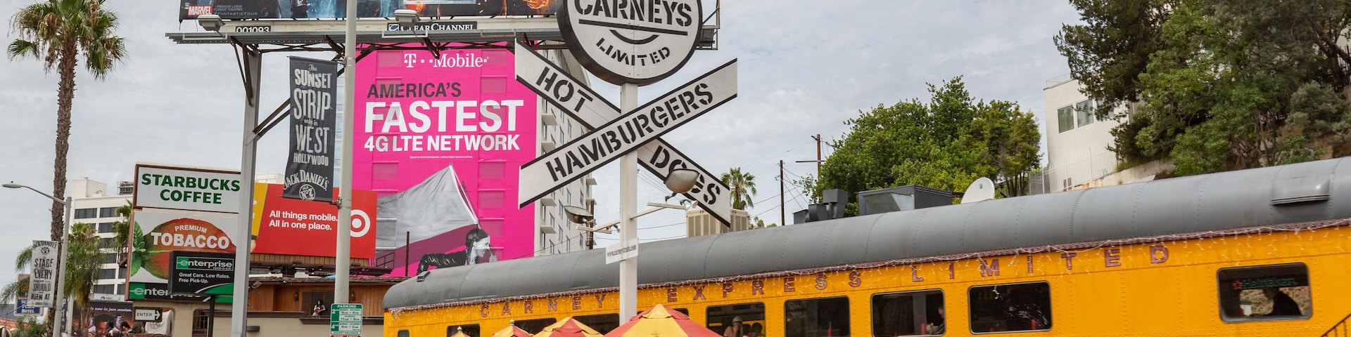 A busy street with a yellow train, a billboard for Marvel's FANT4ST, and a sign for Carneys.