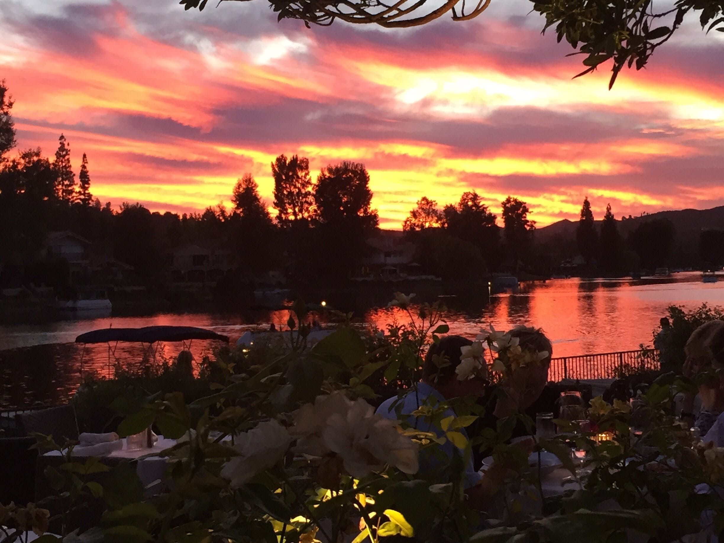 A sunset over a lake with trees and houses in the background.