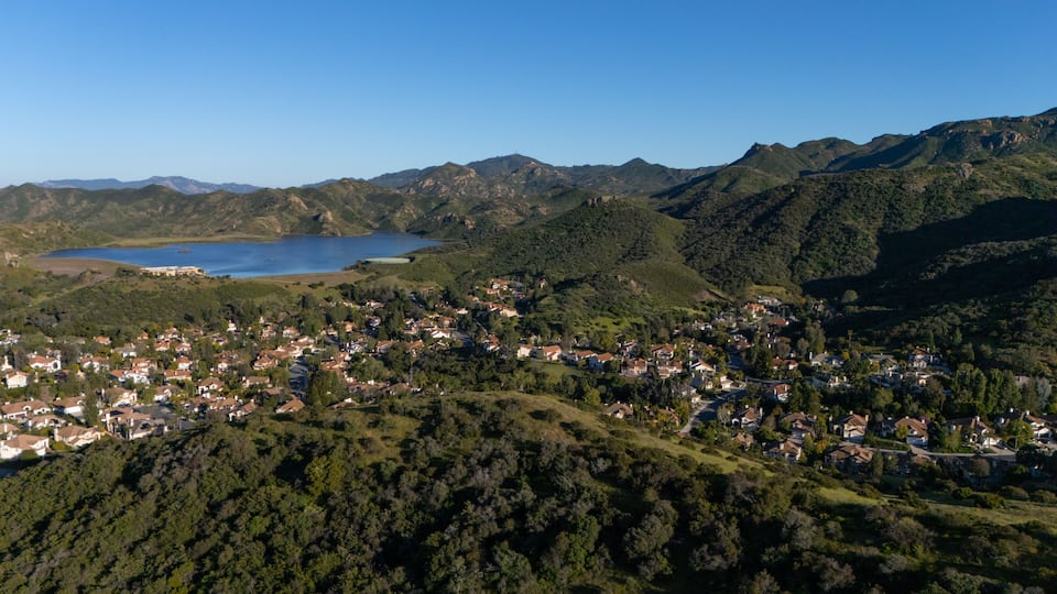 A coastal town nestled between green hills and a large body of water.