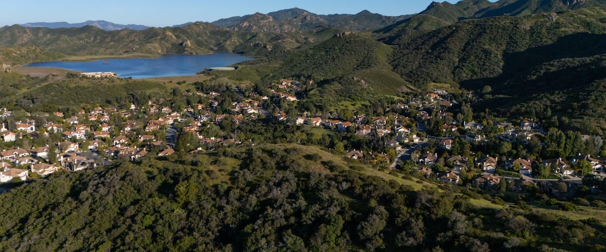 A coastal town nestled between green hills and a large body of water.
