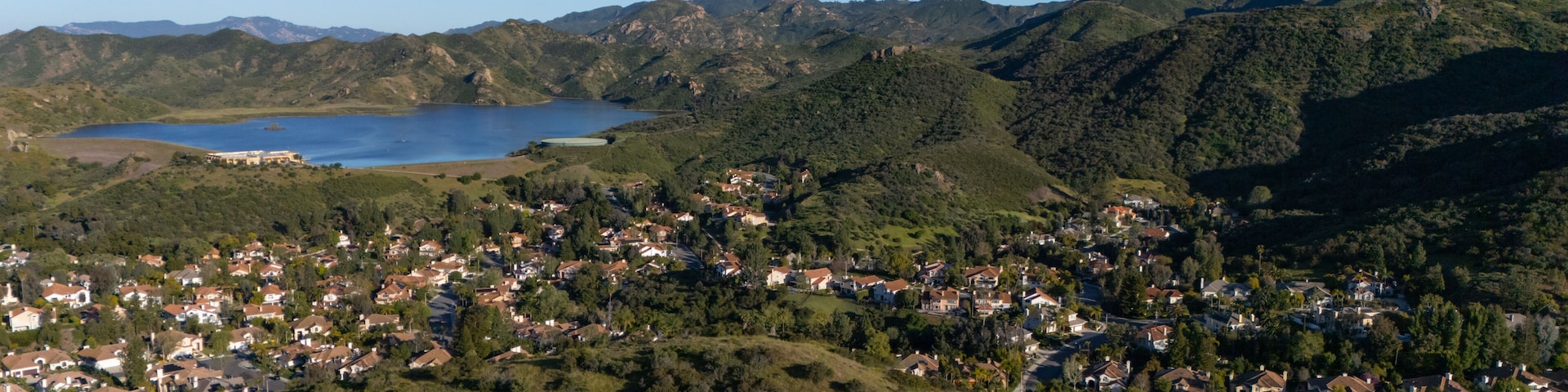 A coastal town nestled between green hills and a large body of water.