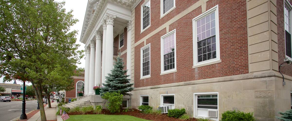 A red brick building with white columns and a green lawn with pink flowers.