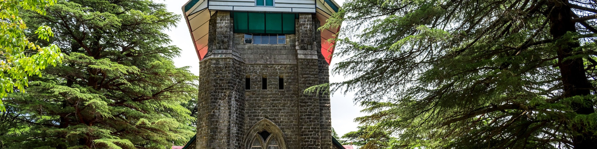A church with a steeply pitched roof, a cross at the top, and a large arched window.