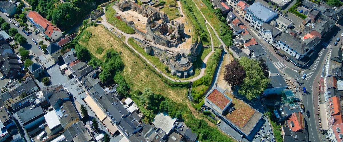 An aerial view of a historic site with ruins, surrounded by modern buildings and roads.