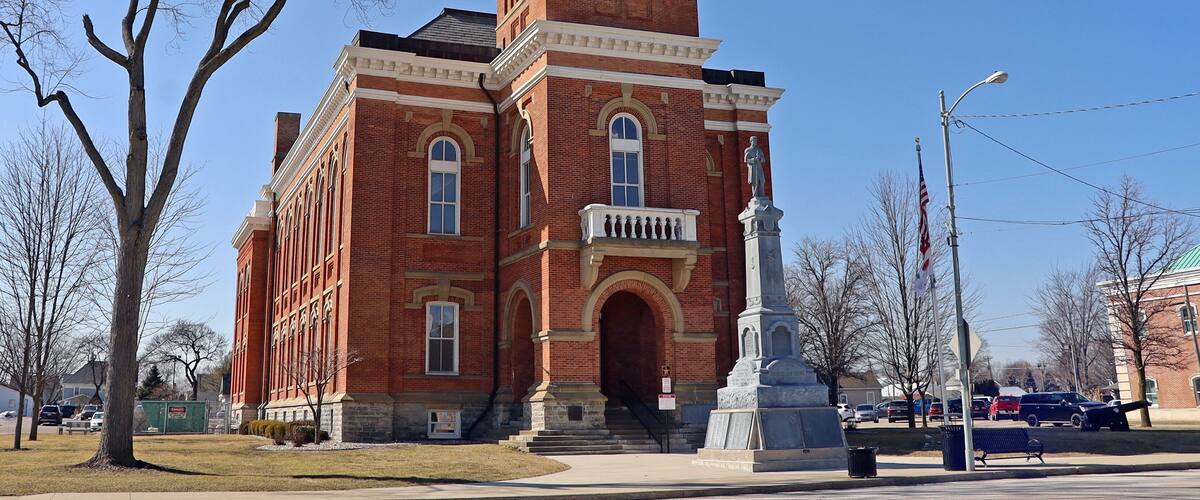 A red brick building with a clock tower and a statue in front.