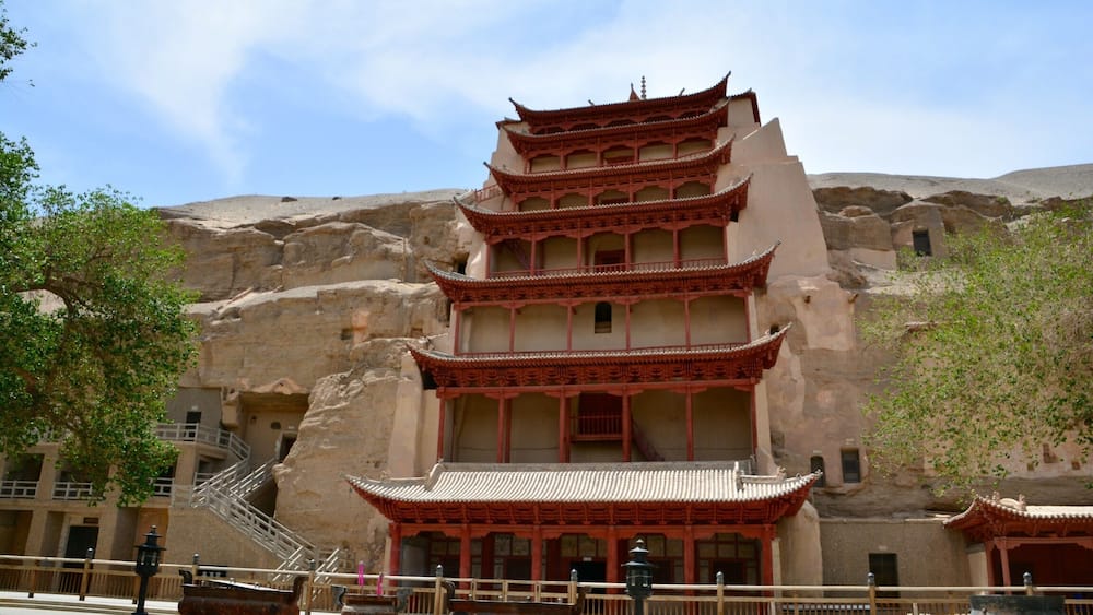 A traditional multi-tiered building with red accents, set against a rocky hillside.