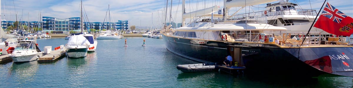 Un port de plaisance où sont amarrés plusieurs voiliers, un grand yacht baptisé « ASAHI », et un bâtiment à la façade bleue en arrière-plan.