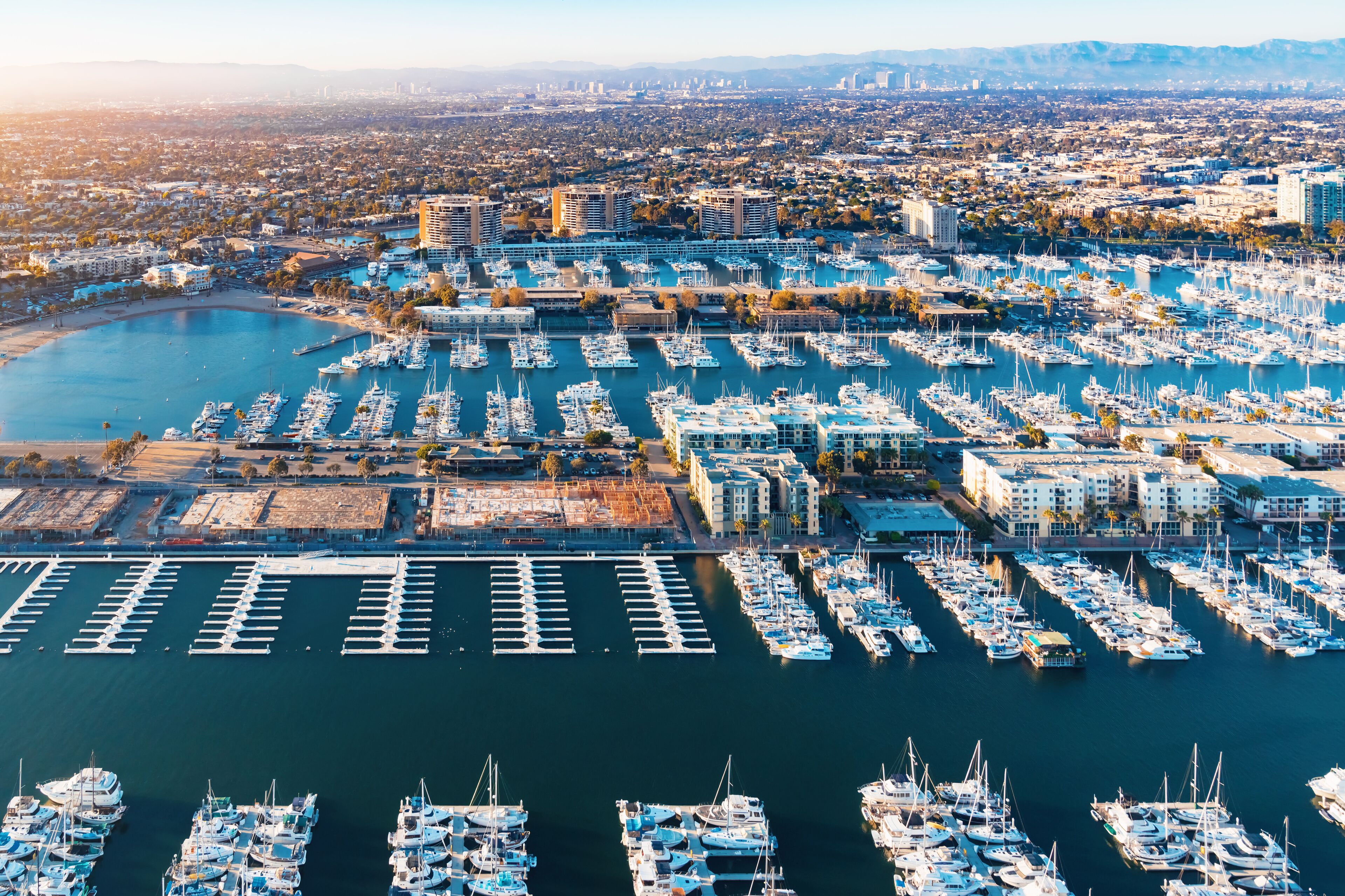 A marina with numerous boats docked, surrounded by urban buildings and a large body of water.