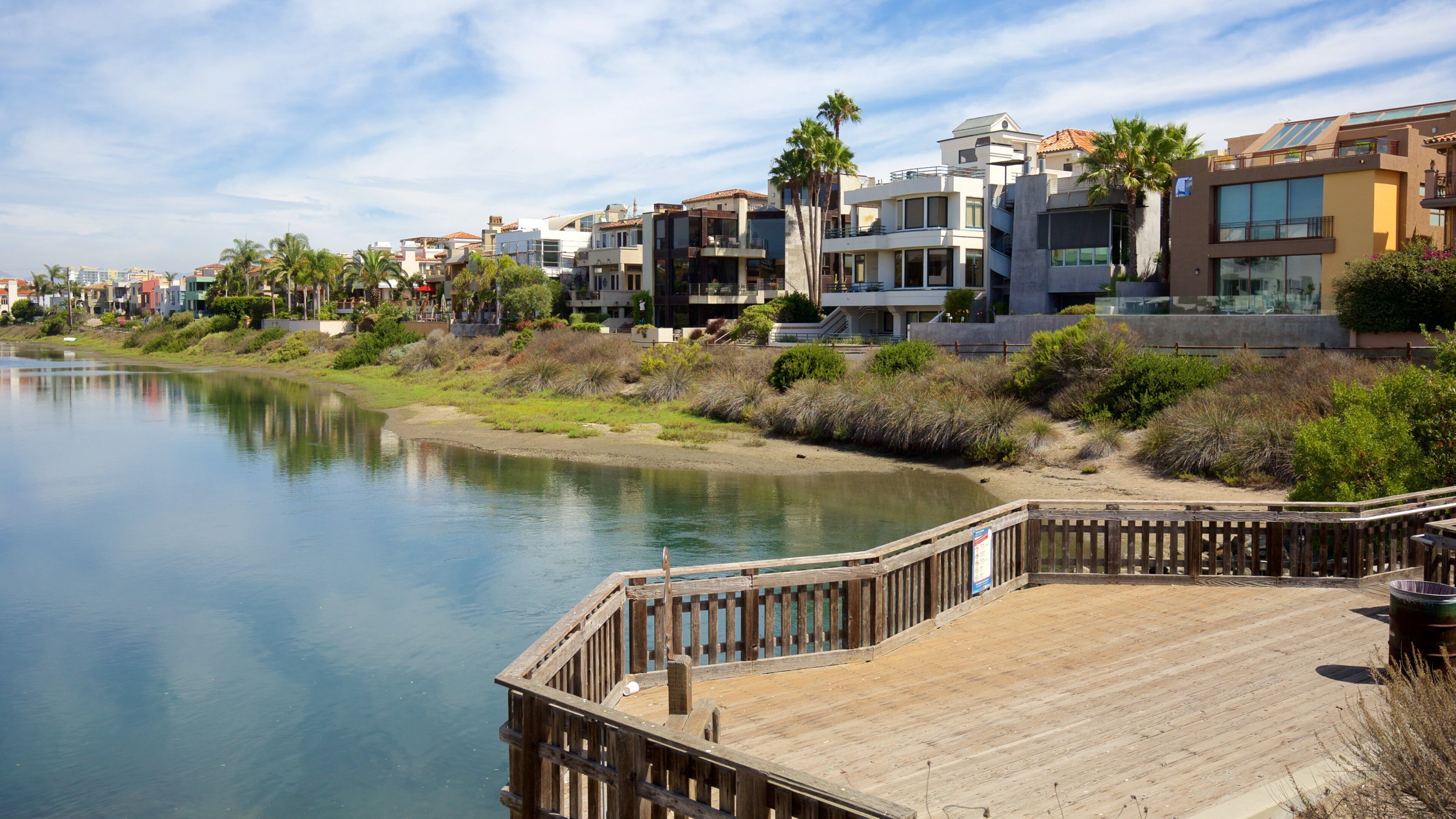 A waterfront with modern buildings, a wooden dock, and a calm river.