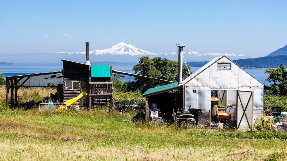 A rustic wooden structure with a green roof and a yellow slide, a metal shed, and a mountain in the background.