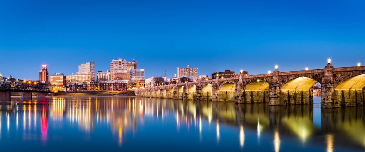 A city skyline at dusk with a historic bridge spanning a calm river.