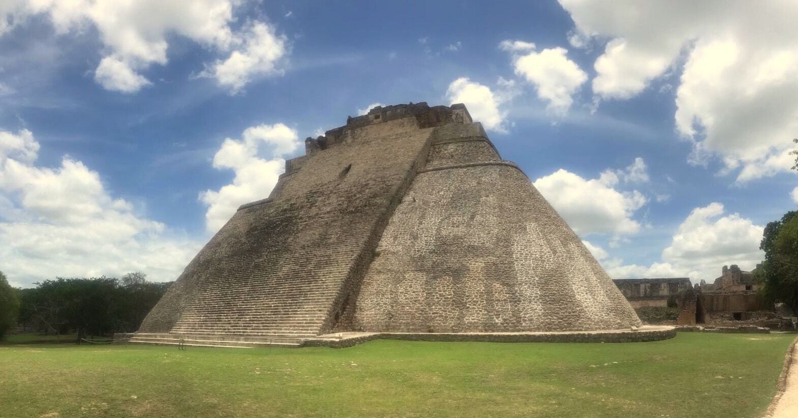 A large pyramid structure with a flat top and steep sides, surrounded by a grassy area and trees.