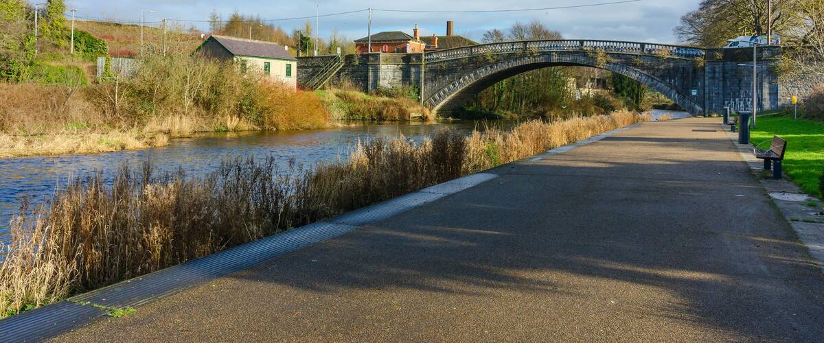 A stone bridge over a river, a paved path, and a bench.