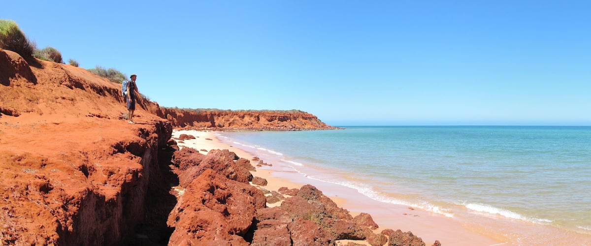 A coastal landscape with red cliffs and a sandy beach.