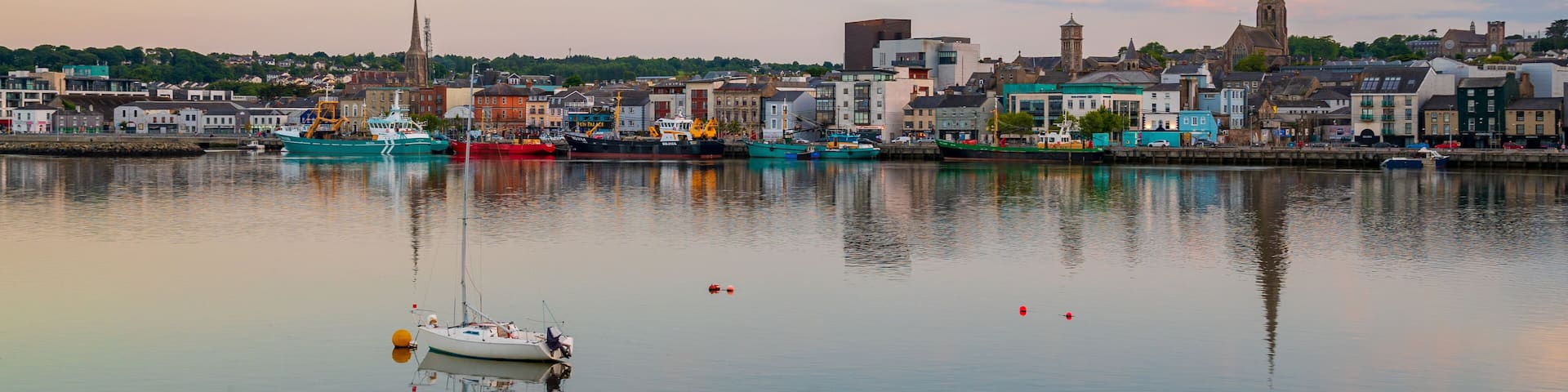 A harbor with boats, a church spire, and buildings along the waterfront.