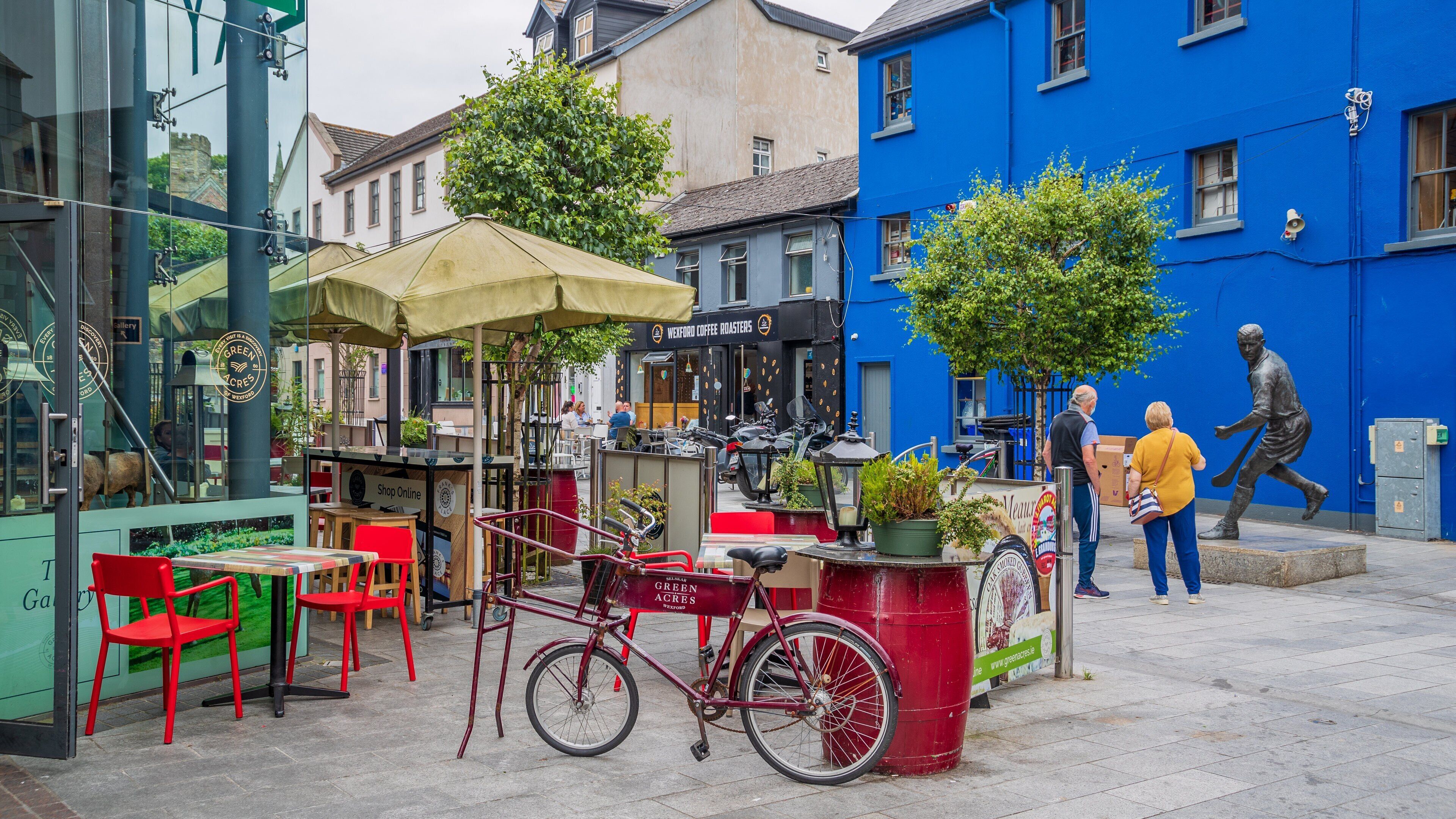 A street food stall with a bicycle, red chairs, and a blue building in the background.