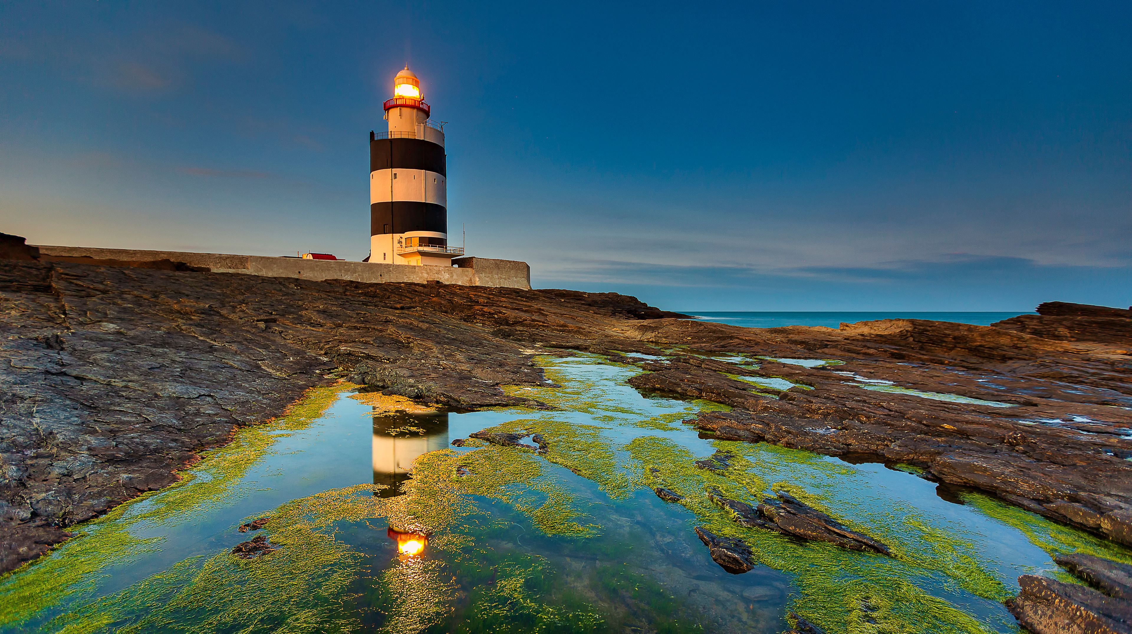 A lighthouse on a rocky shore with algae-covered water.