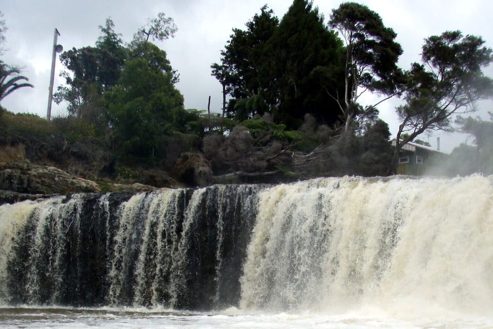 Una canoa en una orilla embarrada con una cascada al fondo.
