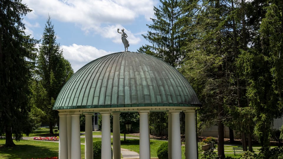 A gazebo with a dome roof, surrounded by a well-manicured lawn and red flowers.