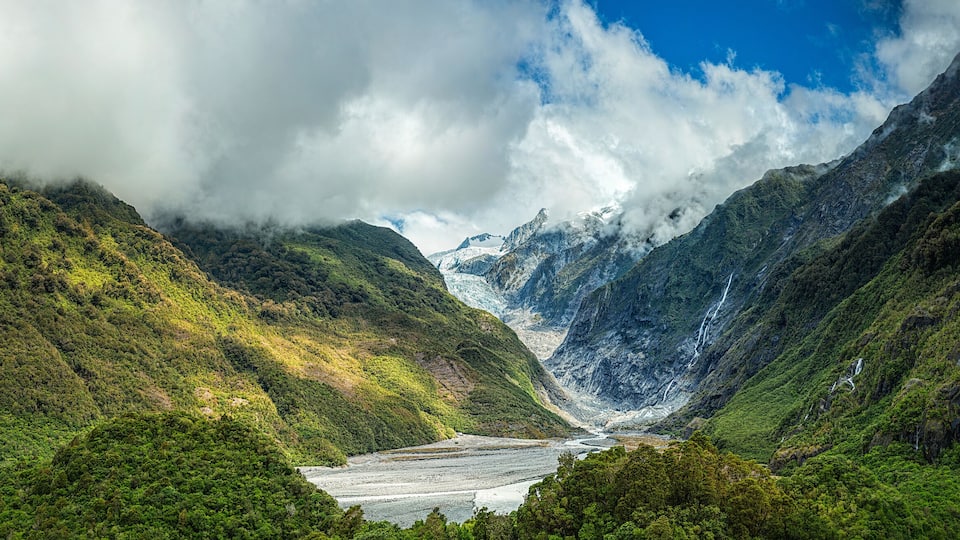 A glacier valley surrounded by lush green mountains and waterfalls.