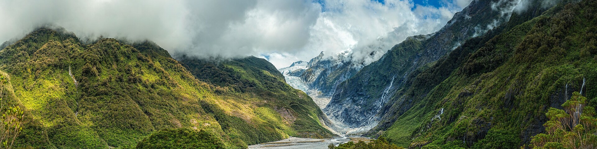 A glacier valley surrounded by lush green mountains and waterfalls.