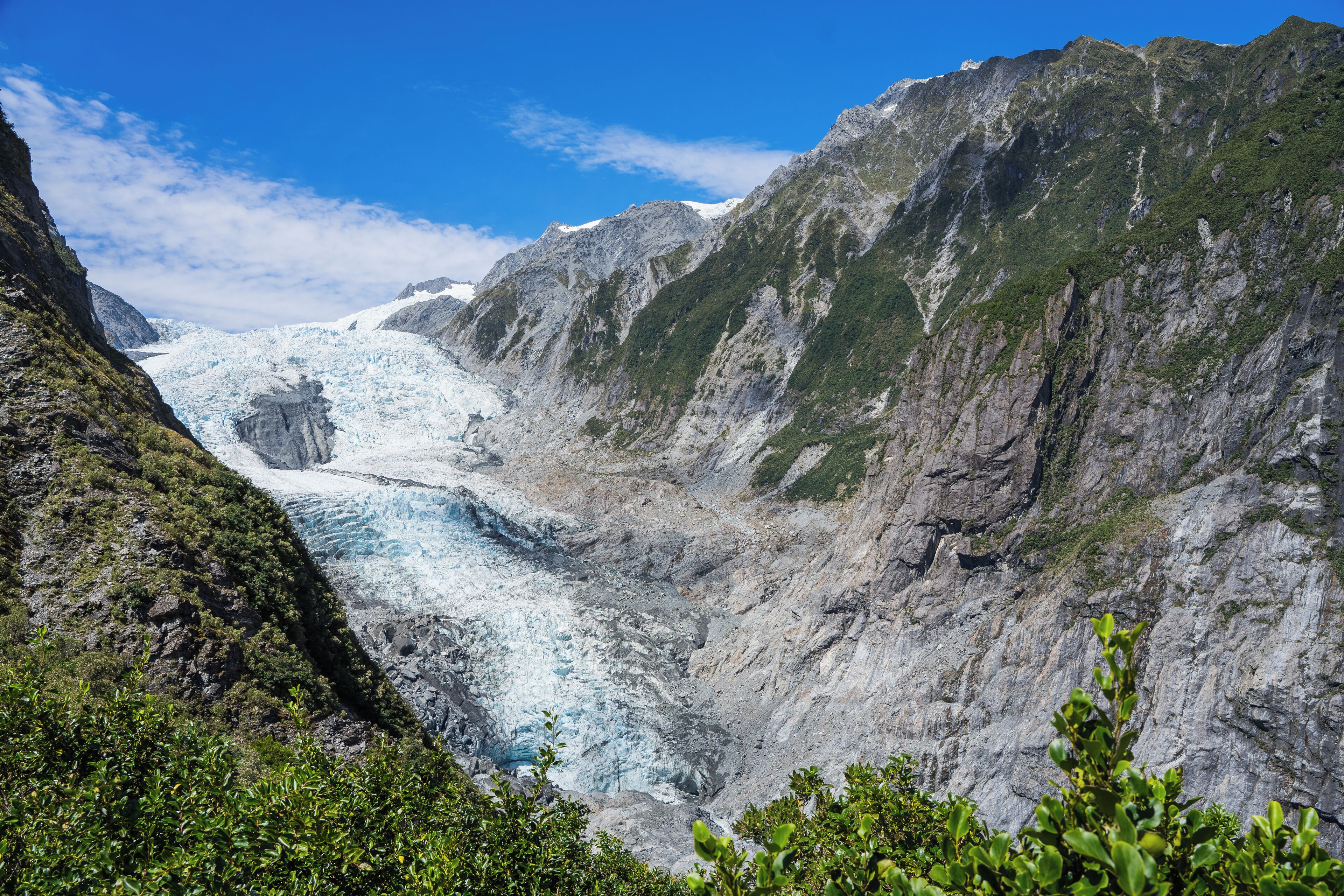 A glacier valley with steep, rocky mountains and lush greenery.