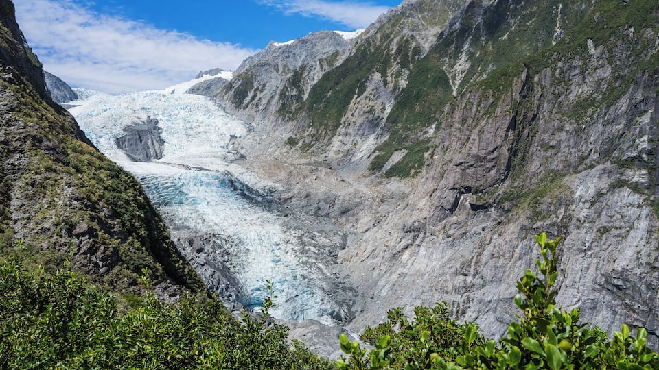 A glacier valley with steep, rocky mountains and lush greenery.