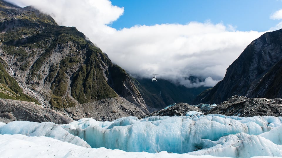 A glacier with a helicopter flying above it.
