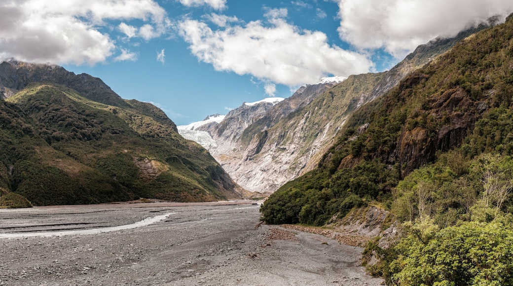 Panoramic view of the alluvial bed of the Waiho River flowing from the Franz Josef Glacier and snow capped mountains in New Zealand