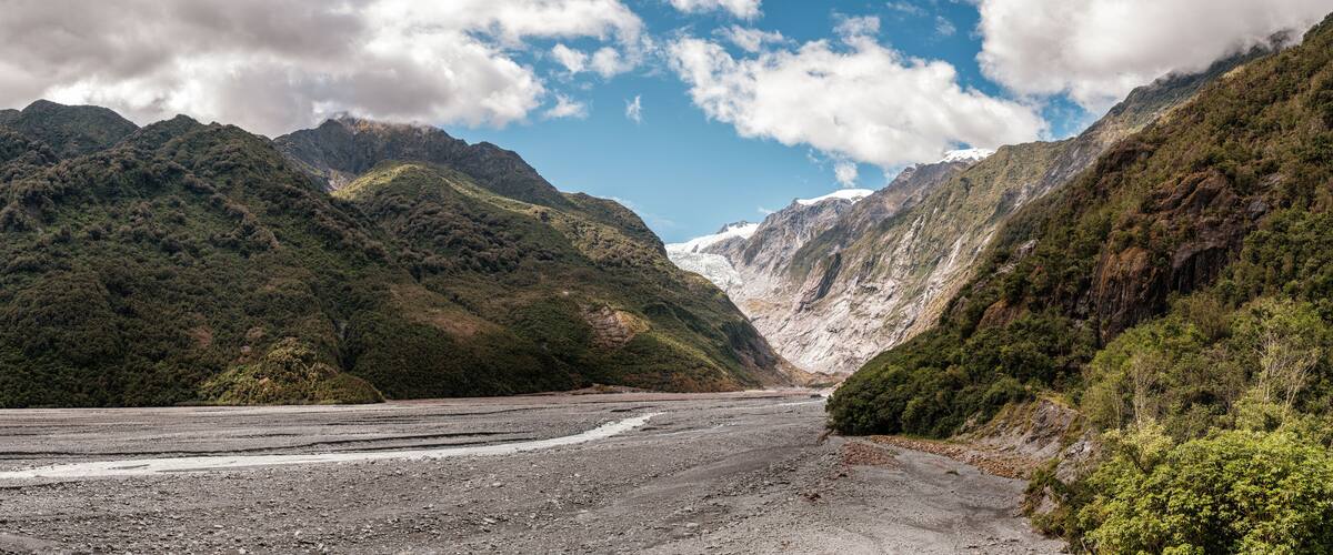 Panoramic view of the alluvial bed of the Waiho River flowing from the Franz Josef Glacier and snow capped mountains in New Zealand
