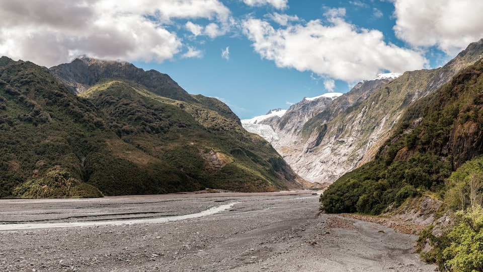 A glacier valley with steep, forested mountains and a clear sky.