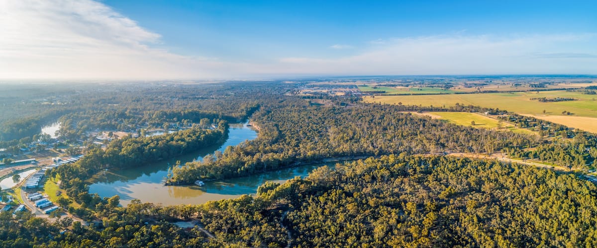 A river winding through a densely forested area with a small settlement and industrial buildings along its banks.
