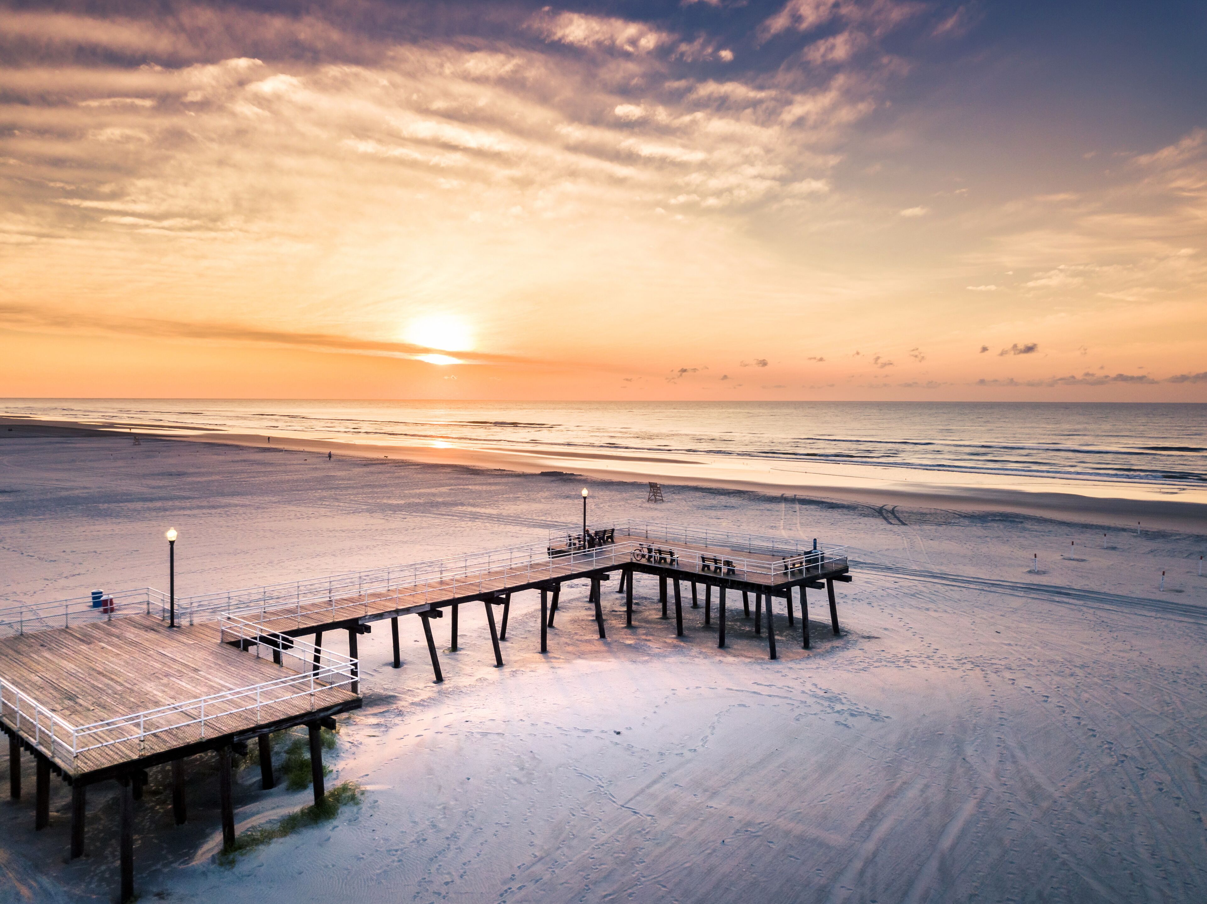 A wooden pier extending into a beach at sunset.