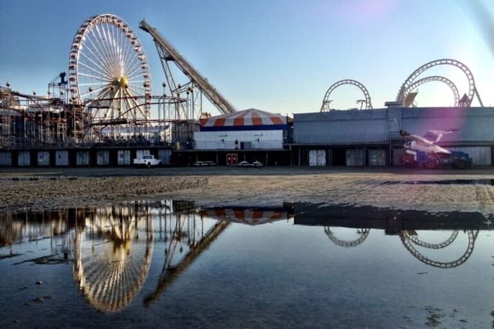 A Ferris wheel, roller coaster, and amusement park buildings by a body of water.