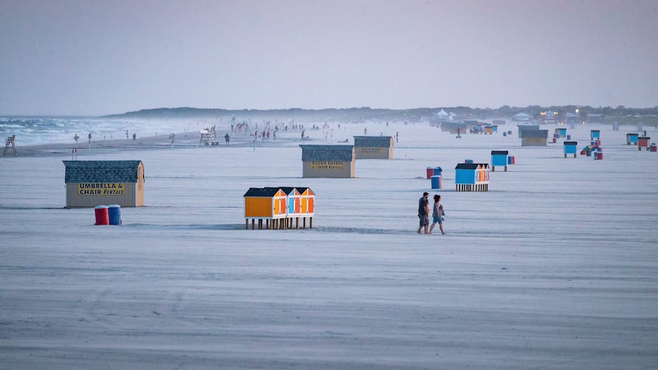 A beach with beach huts and umbrellas.