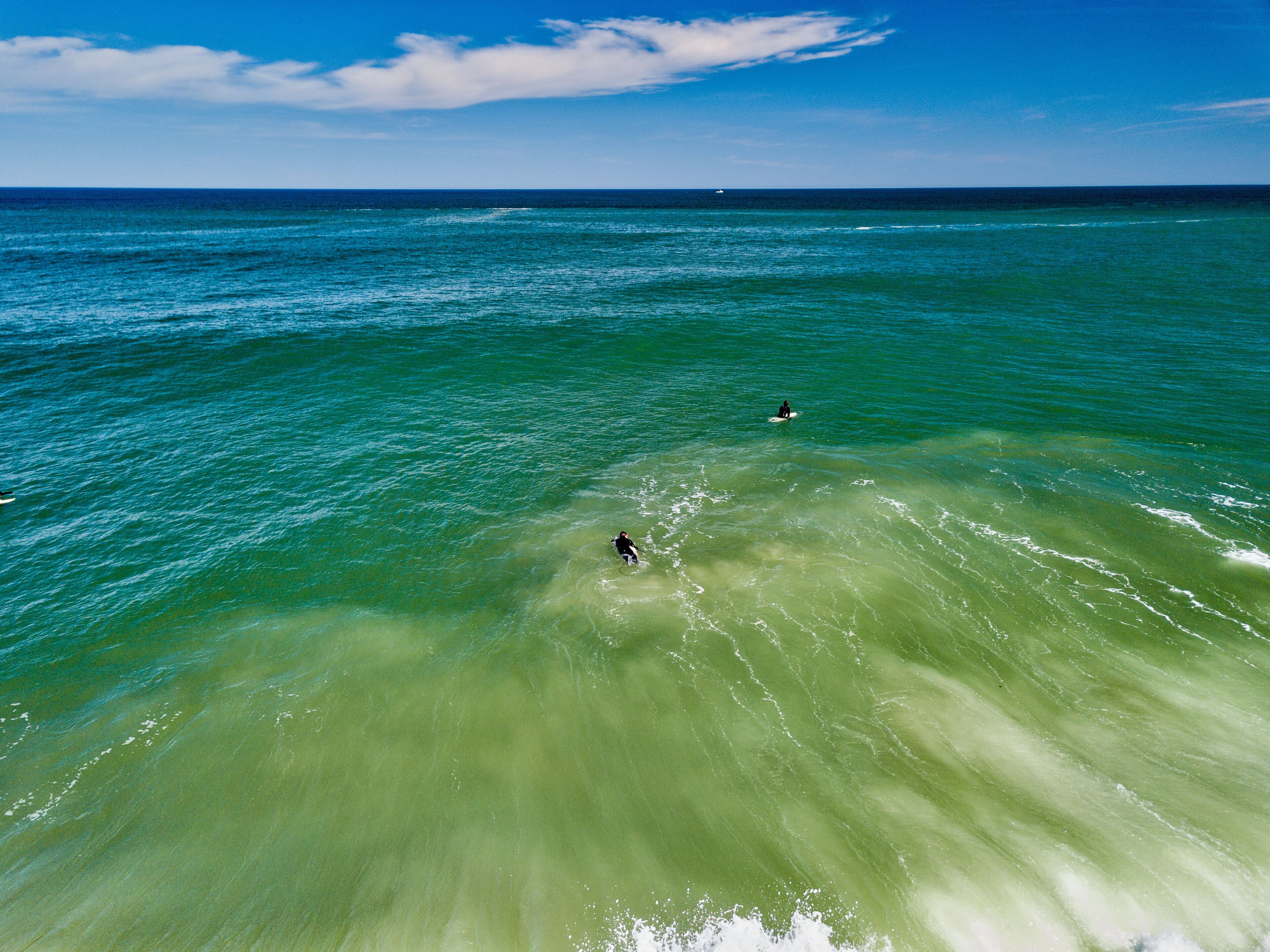 Oceano azul e límpido com dois surfistas.